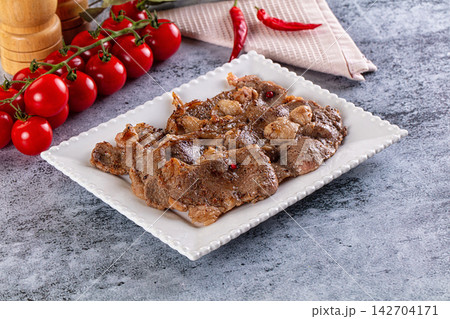 Grilled beef slices with garlic and red peppercorns on white ceramic plate, cherry tomatoes and chili peppers in background Grilled beef slices with garlic and red peppercorns on white ceramic plate, cherry tomatoes and chili peppers in background 142704171