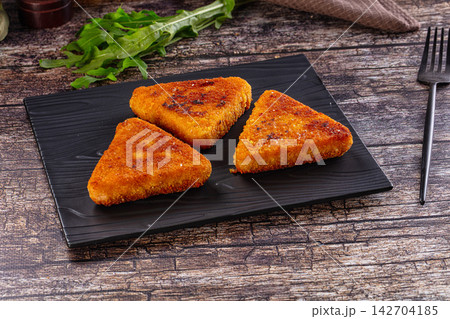 Crispy golden breaded triangular cutlets on black textured plate with fresh arugula on rustic wood background Crispy golden breaded triangular cutlets on black textured plate with fresh arugula on rustic wood background 142704185