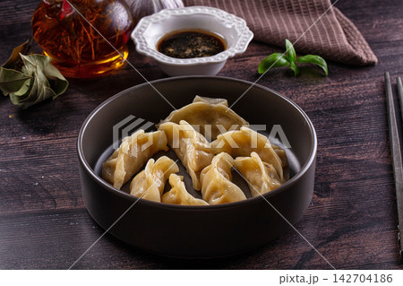 Steaming dumplings in dark bowl with soy sauce, basil, garlic and chili oil on rustic wooden table Steaming dumplings in dark bowl with soy sauce, basil, garlic and chili oil on rustic wooden table 142704186
