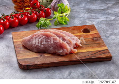 Raw turkey breast slices on wooden cutting board with cherry tomatoes, garlic, celery and olive oil in background Raw turkey breast slices on wooden cutting board with cherry tomatoes, garlic, celery and olive oil in background 142704187