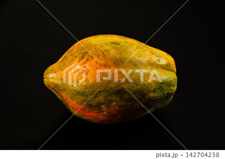 Ripe papaya with yellow green orange skin on black background, shallow depth of field, studio lighting highlighting texture and natural blemishes Ripe papaya with yellow green orange skin on black background, shallow depth of field, studio lighting highlighting texture and natural blemishes 142704238