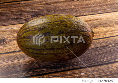 Ripe melon with mottled green and brown rind resting on rustic wooden surface, natural lighting highlights texture and organic imperfections 142704251