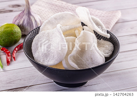 Crispy white pork rinds in black ceramic bowl with garlic lime and red chili peppers on rustic white wood table 142704263