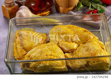 Raw chicken thighs marinated in yellow curry spices in a glass baking dish Raw chicken thighs marinated in yellow curry spices in a glass baking dish 142704298