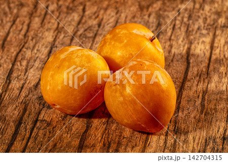 Three yellow plums resting on rustic wooden surface, warm lighting highlighting glossy skin and natural texture Three yellow plums resting on rustic wooden surface, warm lighting highlighting glossy skin and natural texture 142704315