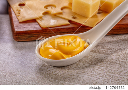 Creamy Yellow Cheese Sauce in Spoon with Various Cheeses on Wood Board Creamy Yellow Cheese Sauce in Spoon with Various Cheeses on Wood Board 142704381