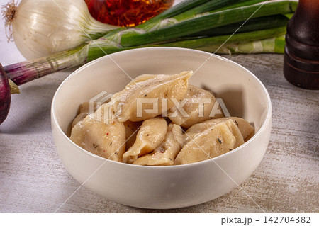 Homemade vareniki dumplings in white bowl with green onions and spices Homemade vareniki dumplings in white bowl with green onions and spices 142704382