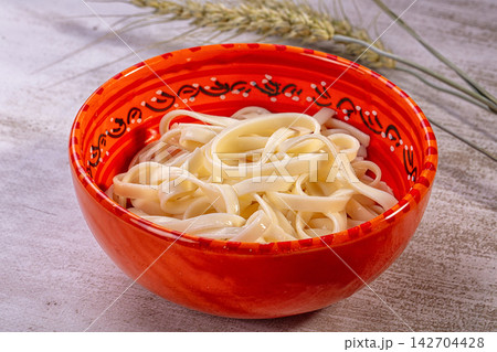 Udon noodles in vibrant red ceramic bowl with black and white decorative pattern, set on textured surface with wheat stalks in background Udon noodles in vibrant red ceramic bowl with black and white decorative pattern, set on textured surface with wheat stalks in background 142704428