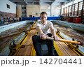 Focused male rower applying strength and endurance during demanding indoor rowing tank workout 142704441