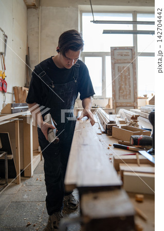 Thoughtful master carpenter checking surface of wooden frame after processing detail with hand plane Thoughtful master carpenter checking surface of wooden frame after processing detail with hand plane 142704442