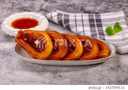 Crispy golden churros dusted with cinnamon sugar served on ceramic plate with red dipping sauce and mint garnish on checkered napkin Crispy golden churros dusted with cinnamon sugar served on ceramic plate with red dipping sauce and mint garnish on checkered napkin 142704511
