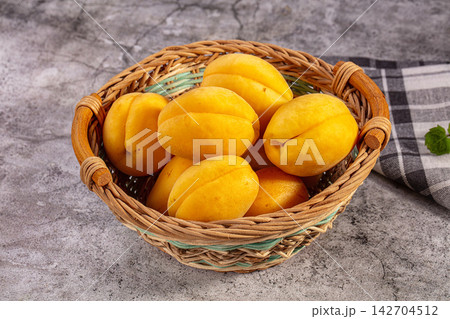 Fresh shalakh apricots in woven basket on textured gray surface with checkered cloth and mint leaf accent Fresh shalakh apricots in woven basket on textured gray surface with checkered cloth and mint leaf accent 142704512