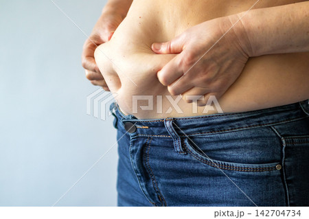 Woman pinching belly fat above denim jeans, body image and weight concern 142704734