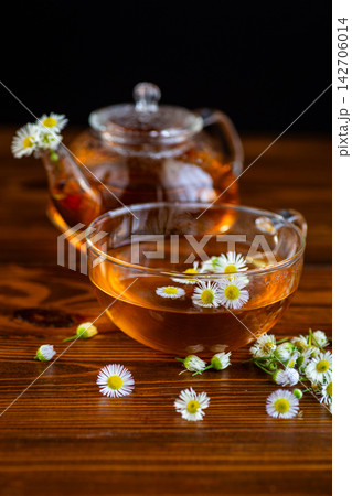 Warm chamomile infusion with glass teapot and flowers on rustic wooden table Warm chamomile infusion with glass teapot and flowers on rustic wooden table 142706014
