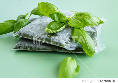 Preserved basil in vacuum bags with fresh leaves on green background 142706016