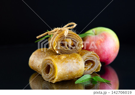 Natural apple fruit leather spirals with ripe apple against dark background Natural apple fruit leather spirals with ripe apple against dark background 142706019