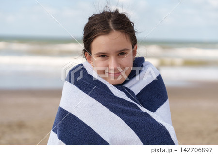 Teen girl wrapped in beach towel looking at camera by sea 142706897