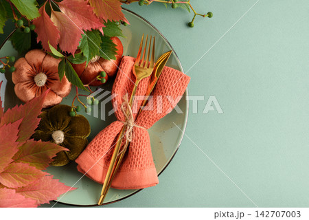 Autumnal harvest table setting with decorative pumpkins and golden cutlery on a plate 142707003
