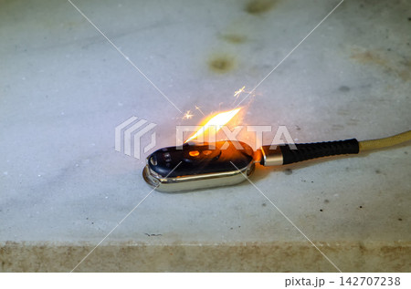 Burning smartwatch connected to cable lies on surface during device fire incident 142707238