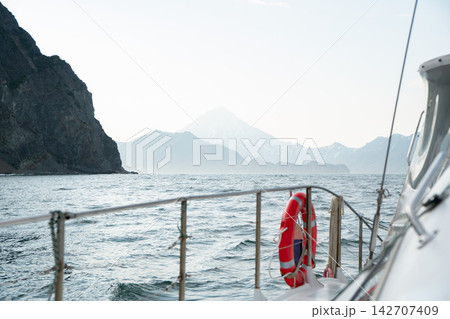 View from a boat along rugged Kamchatka coast with distant mountains fading into soft haze. Marine journey, remote wilderness, scenic exploration, adventure travel and peaceful nature. 142707409