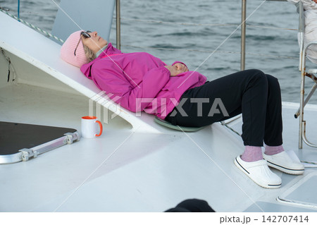 Woman rests and sleeps on catamaran deck while experiencing seasickness and drowsiness after taking motion sickness medication. Travel health, medication side effect, fatigue and marine journey Woman rests and sleeps on catamaran deck while experiencing seasickness and drowsiness after taking motion sickness medication. Travel health, medication side effect, fatigue and marine journey 142707414