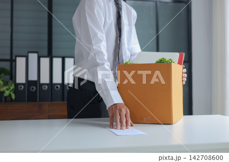Business professional submitting resignation letter and holding packed of personal belongings in cardboard on a desk. Concept of job resignation or termination. 142708600