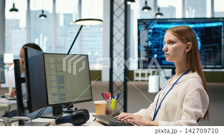 Female technician coding with AI language model assistance in startup office, using PC. Intern using computer, integrating artificial intelligence LLM assistant suggestions into code editor, camera A Female technician coding with AI language model assistance in startup office, using PC. Intern using computer, integrating artificial intelligence LLM assistant suggestions into code editor, camera A 142709710