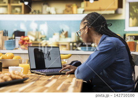Casual black woman looking at new phone product announcement on laptop, interest and curiosity for new technology on gadget. High tech release coming soon, innovative technology news. 142710100