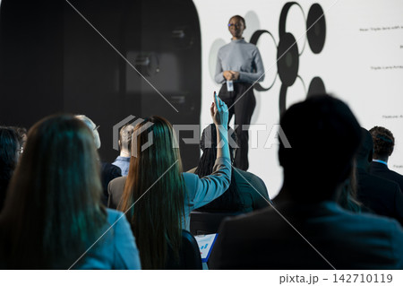 Participant asking questions about new phone launch presentation in auditorium, raising hand and interacting with black product manager on stage. Audience engagement at reveal. 142710119