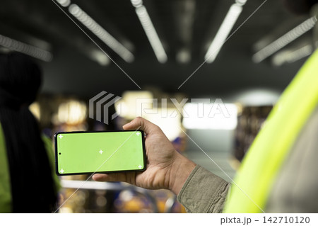 Green screen phone with staff working in warehouse storage facility, coordinating loading and unloading processes with coworker. Shipping operations and order fulfillment in stock industry. Green screen phone with staff working in warehouse storage facility, coordinating loading and unloading processes with coworker. Shipping operations and order fulfillment in stock industry. 142710120