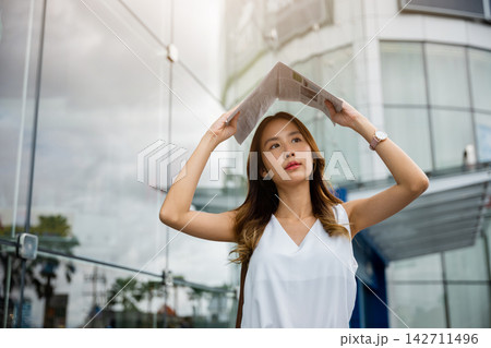Overwhelmed by city living, an Asian woman covers her face with a newspaper 142711496