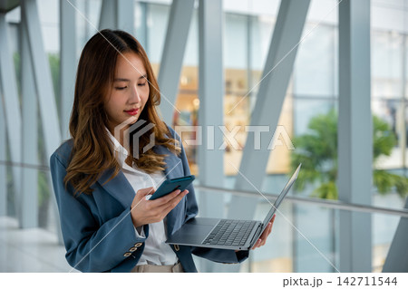 Digital nomad working remotely with laptop and cell phone in airport 142711544