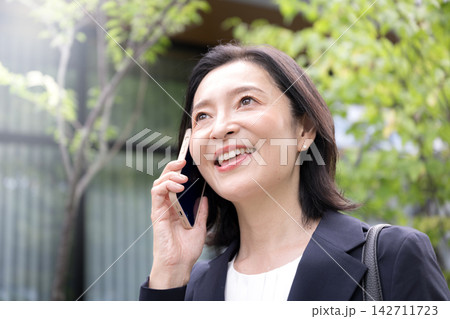 屋外でスマホを使って電話する50代のビジネスウーマン、外出先で仕事の連絡をする働く女性クローズアップ 142711723