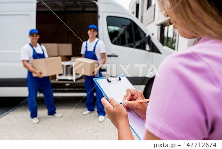 Two removal company workers unloading boxes from minibus into customer's home 142712674