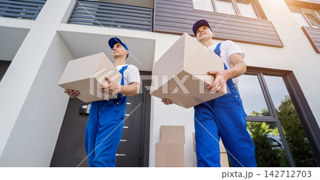 Two removal company workers are loading boxes and furniture into a minibus. 142712703