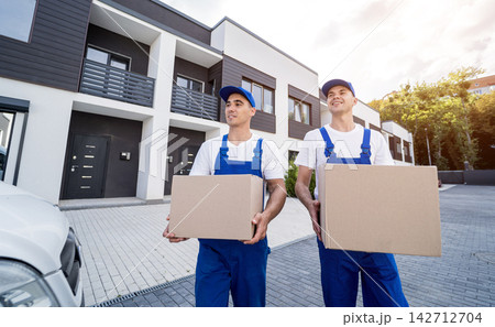 Two removal company workers are loading boxes and furniture into a minibus. Two removal company workers are loading boxes and furniture into a minibus. 142712704