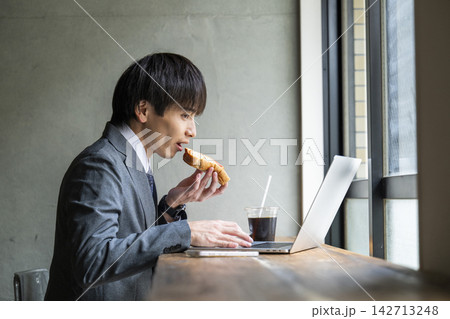 カフェでトーストを食べながら仕事をするビジネスマン カフェでトーストを食べながら仕事をするビジネスマン 142713248