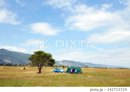 Camping in a large field with a car, tent, tree, and mountains in the background. Camping in a large field with a car, tent, tree, and mountains in the background. 142713729