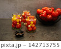 Red and yellow tomatoes are inside glass jars and a bowl on a dark kitchen counter.  142713755