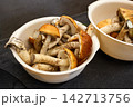 Mushrooms are placed in two white bowls on a dark surface.  142713756