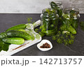 Cucumbers and spices are arranged on a kitchen counter for pickling in glass jars with fresh herbs 142713757