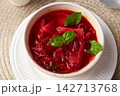 Bowl on a white plate with red soup filled with vegetables.  142713768