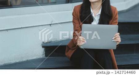 Young professional woman talking on phone and holding coffee outside modern office building Young professional woman talking on phone and holding coffee outside modern office building 142714460