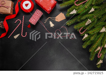 Christmas-themed flat lay arrangement featuring wrapped gifts, decorative ribbons, candy canes, and a pine tree branch on a dark background 142715025