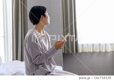 ベッドでスマホを見る女性、窓の外を眺める ベッドでスマホを見る女性、窓の外を眺める 142716370