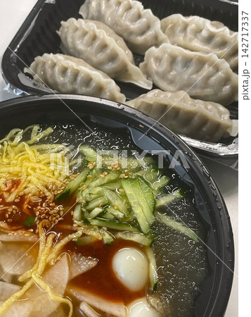 Chilled, chewy naengmyeon noodles in tangy broth paired with juicy, savory mandu dumplings, offering a perfect balance of refreshing coolness and hearty comfort in every delicious Korean bite. 142717337