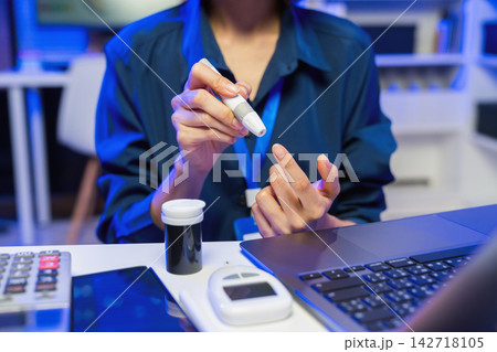 Young Asian woman checks her blood sugar with a glucose meter for diabetes monitoring. 142718105