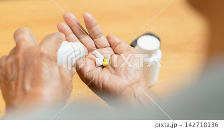 Elderly Asian woman holding medicine in hand at home, medication and senior healthcare. 142718136
