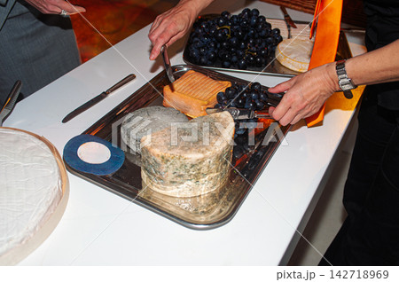Guests Serving Aged Cheese and Grapes on a Silver Platter at a Party Buffet 142718969