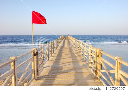 A wooden pier with a red warning flag at sunset. A wooden pier with a red warning flag at sunset. 142720907